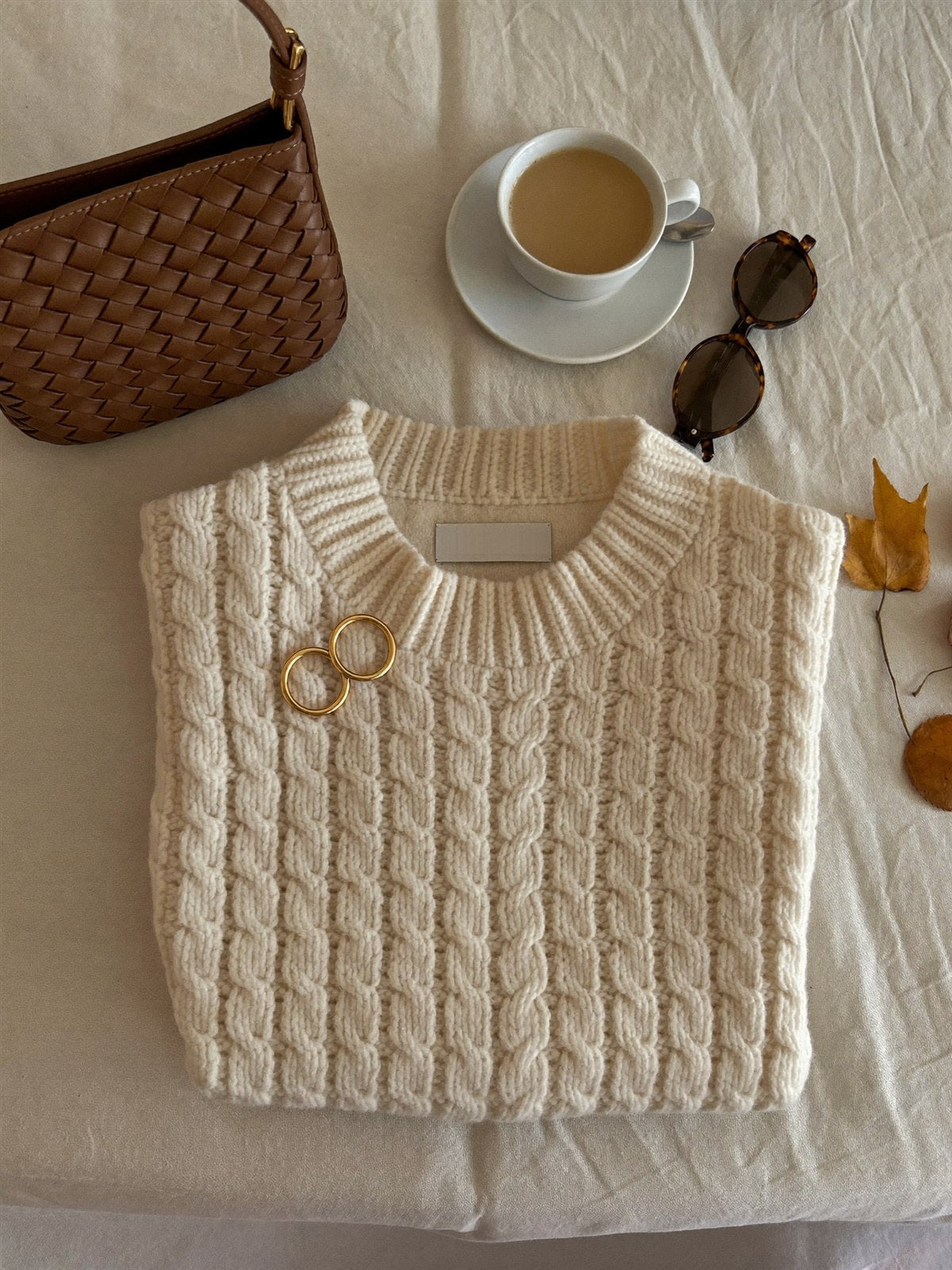 Tricot crème, sac tressé et café au lait sur une nappe de lin